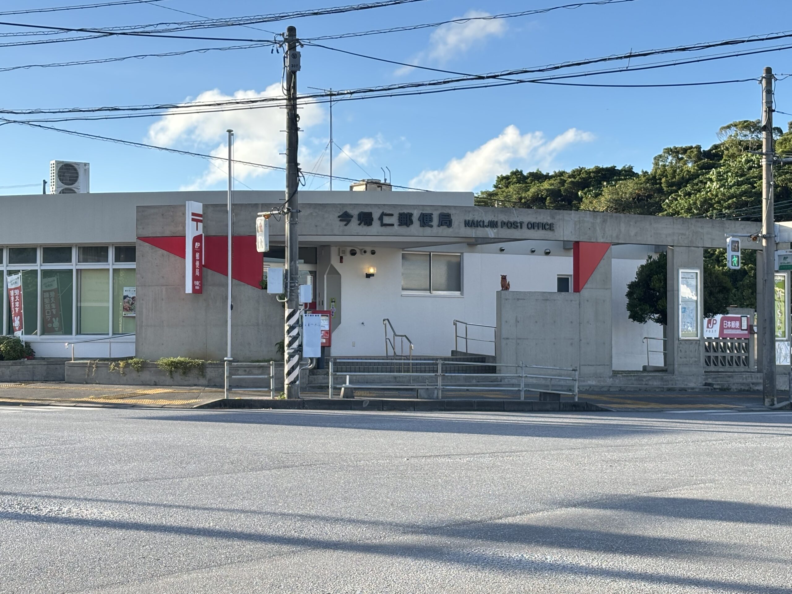 今帰仁郵便局の外観。青空の下、コンクリートの建物とポストが写っている